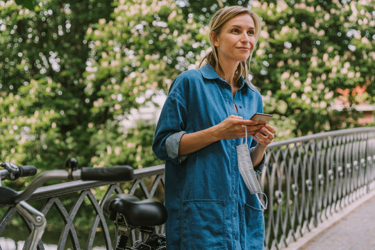 Woman on a bridge with face mask, smartphone and bicycle - Powered by Adobe