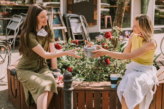 Woman with taken off face mask handing over gift to friend