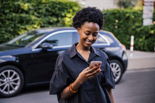 Portrait of smiling young woman standing on the street looking at cell phone