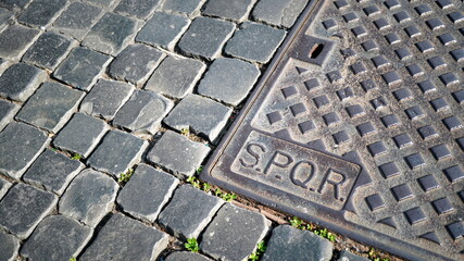Cast iron manhole cover with SPQR engraving on a stone floor with a geometric design in the morning...