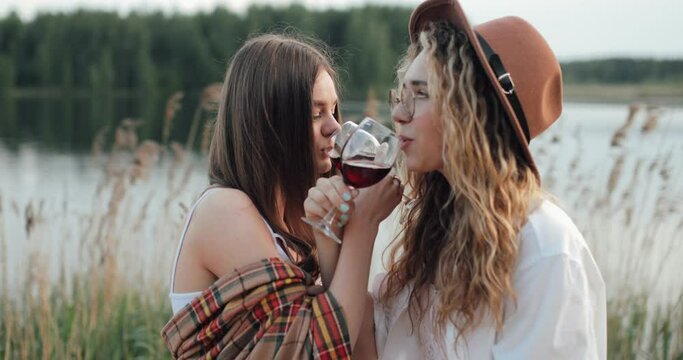two cute lesbians on the background of a lake drinking wine on the bruderschaft