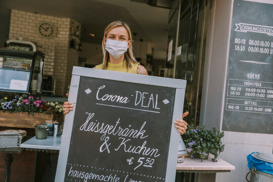 Cafe owner wearing face mask holding a board with Corona special offers