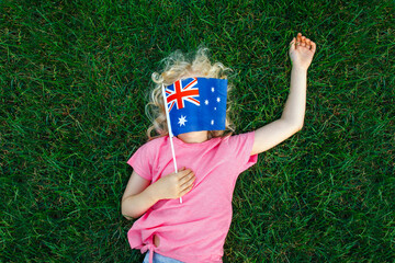Adorable cute happy Caucasian girl holding Australian flag. Funny child kid covering her face with...