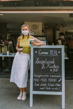 Cafe owner with face mask standing by menu board with Corona special offers