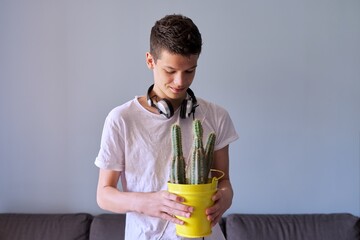 Portrait of teenage boy in headphones holding pot of cacti in his hands