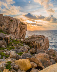 Fototapeta na wymiar Cloud-covered sunset fills the background of a rocky Maltese landscape