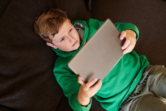Boy using digital tablet while lying on sofa at home