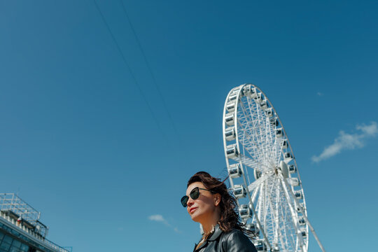 Woman wearing sunglasses near Ferris wheel against blue sky
