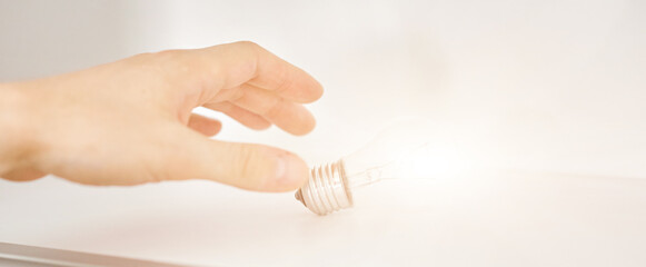 hand reaches for a glowing light bulb on a white shelf. The concept of aspiration behind the idea 
