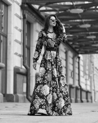 Pretty beautiful caucasian woman with long dark wavy hair wearing black and red colorful ball gown dress and sunglasses. Model standing and posing at city street