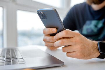 man checks phone while working from home, remotely, behind laptop