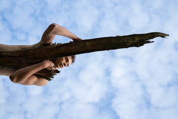 Low angle view of man sleeping on log against cloudy sky in forest