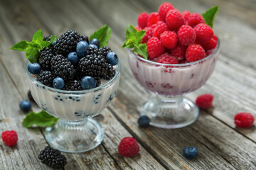 Dessert of cream, raspberries, blueberries and blackberries in glass vases on a wooden background.
