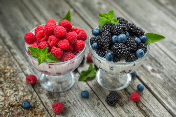 Dessert of cream, raspberries, blueberries and blackberries in glass vases on a wooden background.