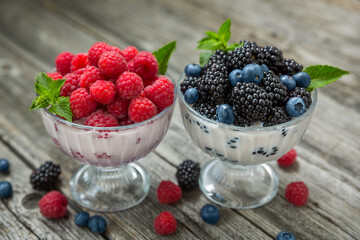 Dessert of cream, raspberries, blueberries and blackberries in glass vases on a wooden background.