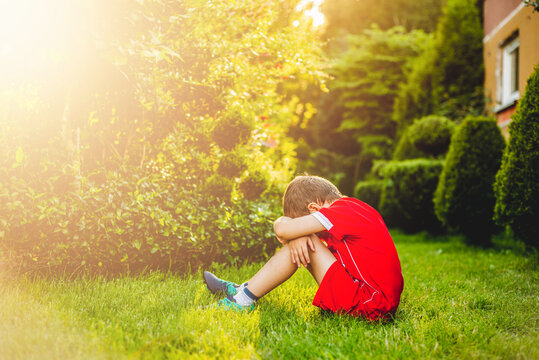 Tired boy after sport. A boy dressed in sports attire sits on the grass tired after playing football.