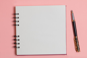 Top view of a blank notepad next to a pen on a pink background.