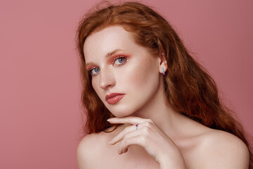 Beautiful redhead freckled woman with bold pink eyes makeup, wearing colorful jewelry: earrings, rings, posing in studio. Jewellery advertising conception. Copy, empty space for text