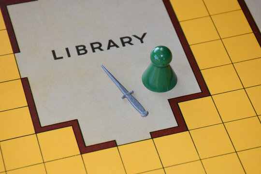 A detail of a board game with a game piece and a dagger , set in a library