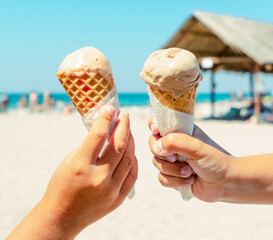 Couple kids hands holding ice cream cones at the beach background in summer vacation. Summer food, summertime joy, vacation, holidays.
