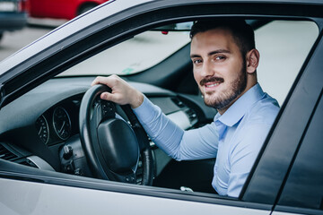  man smiling and sitting in front of the steering wheel in luxury car posing