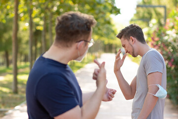 Young man with coronavirus protection mask instructs a young man to put on the mask correctly but he refuses on a park street