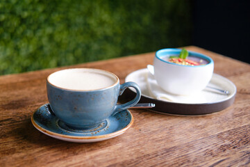 Blue cup of cappuccino coffee on a wooden table. Fruit dessert and drink in a summer cafe, close up