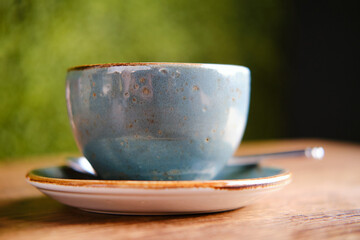 Blue cup, saucer and spoon on a wooden table of a summer cafe, close up