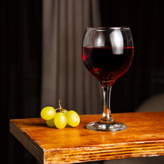 Glass of red wine and grapes on a vintage wooden bar counter with copy space. Shallow depth of field. Blurred background