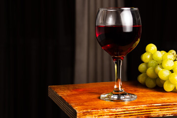 Glass of red wine and grapes on a vintage wooden bar counter with copy space. Shallow depth of field. Blurred background