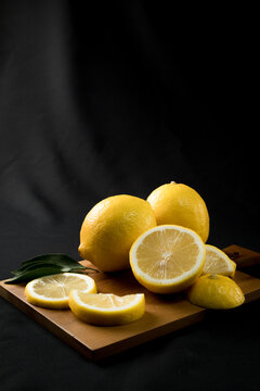 Fresh yellow lemon lime fruit with slices and fresh lemon juice on wood cutting board on black background , Copyspace for text.
