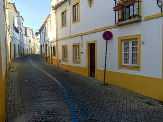 Inviting view of quiet city street in the historic walled city of Evora, Portugal. Yellow and white residential district and quaint winding cobblestone street in natural morning sunlight. Full frame