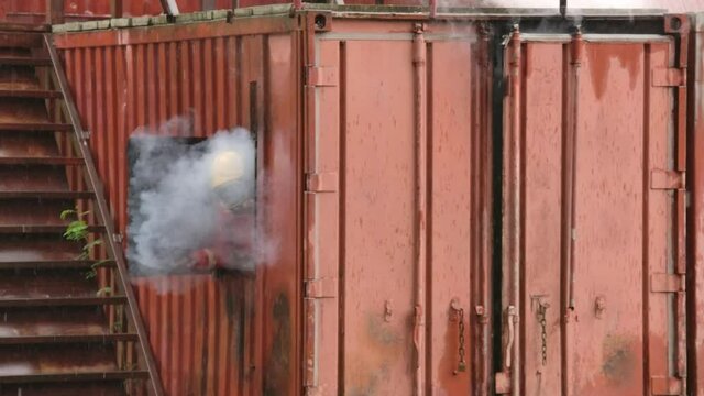 Fireman or firefighter from fire department wearing fire protection suit and helmet and breathing with oxygen tank he open windows with full of smoke.