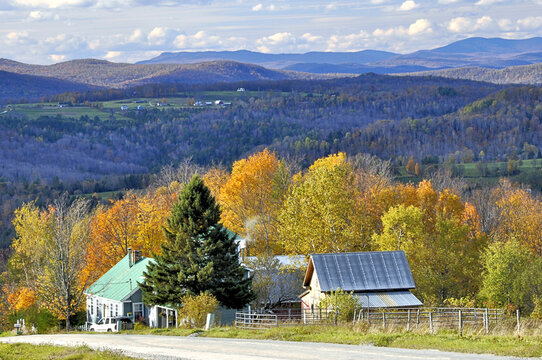 Quiet country road in Northeast Kingdom of rural Vermont with sweeping view of mountains, distant farm, and colorful autumn foliage.