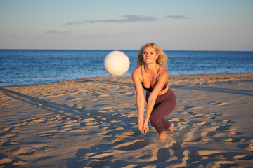 Stunning young blonde woman poses on beach in work-out attire with volleyball - dig