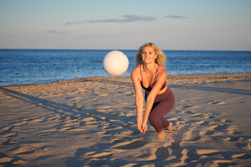Stunning young blonde woman poses on beach in  work-out attire with volleyball  - dig