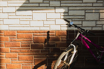The bike stands against the wall of the house, on the brown-beige wall the shadow of the roof of the house.