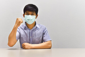 Asian man wearing a mask is sitting and lifting his fists to show strength when protecting against coronavirus.New normal concept.