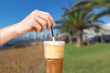 Female hand stirring a straw on a greek cold coffee, freddo cappuccino at a beach.