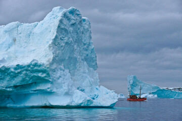 Fototapeta na wymiar Tourists cruise among enormous icebergs on a converted fishing boat out of Ilulissat in West Greenland's Disko Bay.