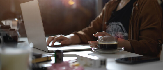Female photographer working with laptop on table with camera, supplies and decorations in studio