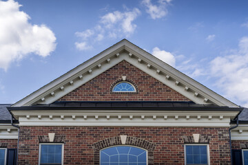 Classic Greek style symmetrical shape gable pediment,decorated cornices and friezes on a new American brick home with blue cloudy sky