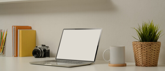 Modern home office with mock up laptop, camera, cup, stationery, books and decorations on white table