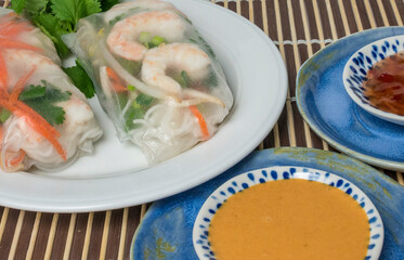 Soft wrap Vietnamese shrimp spring rolls on a plate with bowl of peanut sauce at the side. 