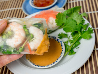 Fresh soft wrap spring roll with shrimp being dipped by hand in sweet peanut sauce. 