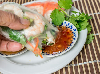 Fresh soft wrap spring roll with shrimp being dipped by hand in sweet chili sauce. 