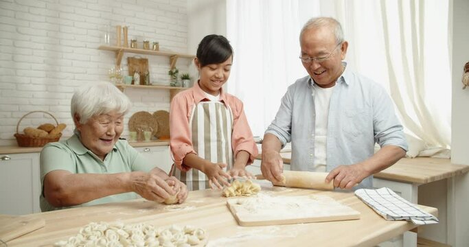 Senior asian couple teaching their teen granddaughter how to prepare dough for dumplings, spending time together - childhood memories, family ties concept 4k footage