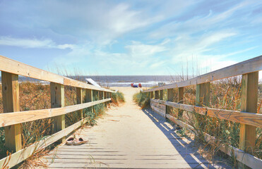 An ocean view down a wooden ramp to a sandy beach in pastel colors.