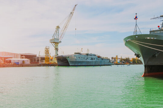 The military ship was waiting to be repair moored alongside in shipyard near floating dock on blue sky.