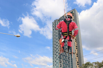 Male rope access and abseiling industry worker wearing safety harness, fall protection helmet hanging working on building background